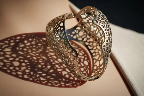 Design de joias artesanais, close-up artístico de um pingente contemporâneo com design vazado e intrincado, onde a luz natural incide e interage com os espaços abertos, criando jogos de sombra e realçando a pele do usuário.