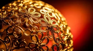 Fios para cloisonné joalheria artesanal, fotografia macro de fios de ouro e prata entrelaçados em padrões orgânicos de arabescos com iluminação dourada intensa e fundo avermelhado.